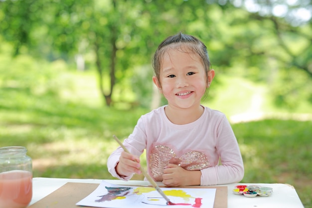 fille enfant asiatique assis à une table dans un jardin d&#39;été peinture au pinceau