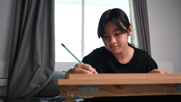 Fille enfant asiatique à faire ses devoirs assis sur le lit à la maison.