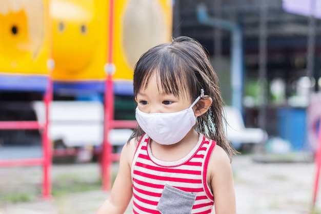 Fille enfant asiatique heureuse souriant et portant un masque en tissu. Elle joue dans la cour de récréation.