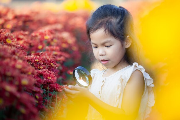 Fille enfant asiatique mignon à la recherche de belles fleurs à travers une loupe dans le champ de fleurs