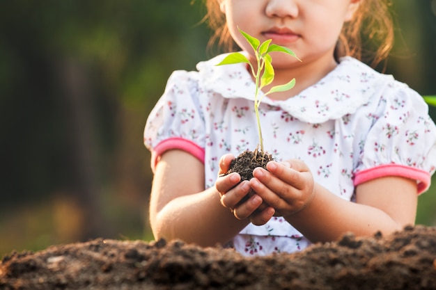 Fille enfant asiatique mignon tenant un jeune arbre pour planter dans le sol noir dans le jardin avec plaisir