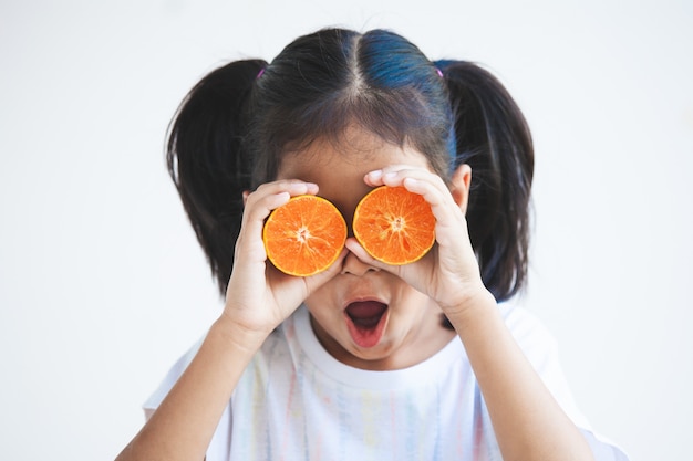 Fille enfant asiatique mignon tenant des oranges fraîches couvrant ses yeux