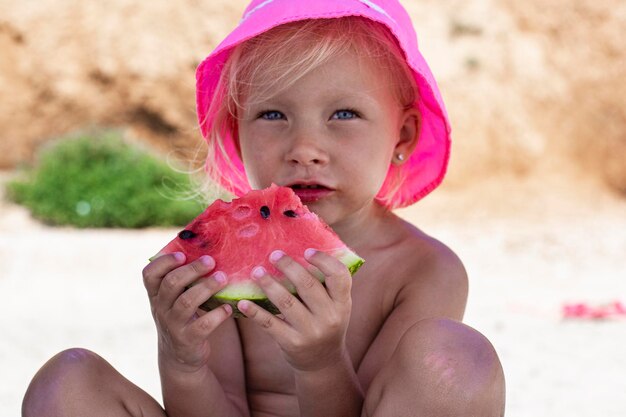 Fille enfant au chapeau de panama mangeant de la pastèque alors qu'il était assis sur la plage.