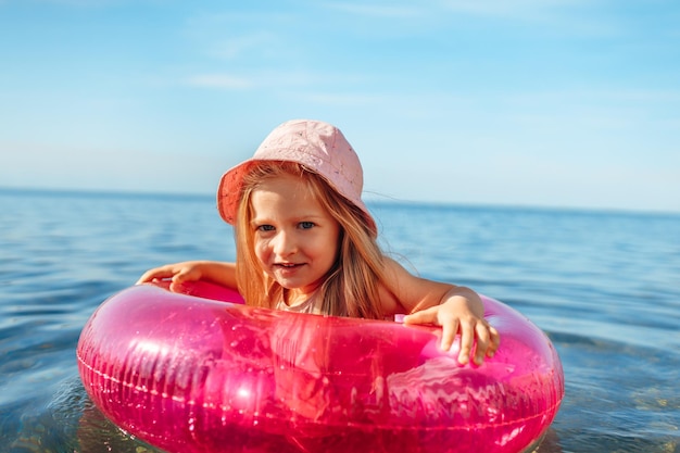 Fille enfant au panama rose nageant en mer avec cercle