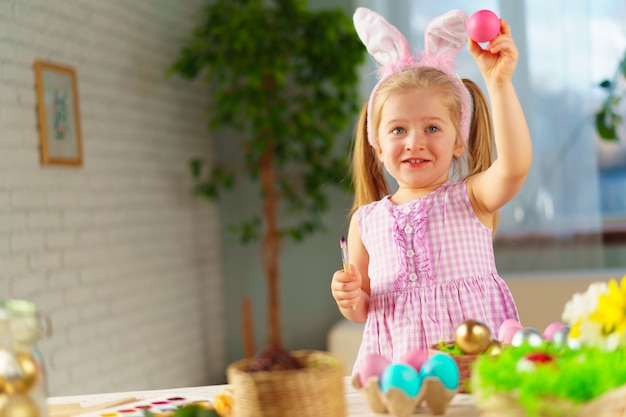 Fille enfant en bas âge avec des oreilles de lapin colorant des oeufs pour Pâques