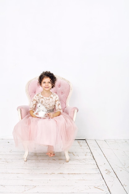 Fille d'enfant belle mignonne gaie et heureuse avec une tasse de thé sur une chaise rose