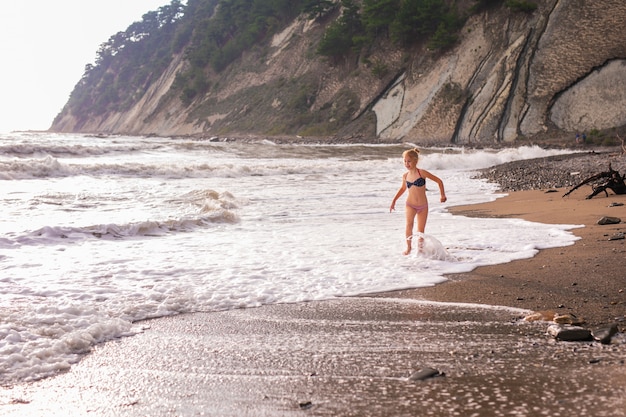 Fille enfant blonde mignonne qui court des vagues de la mer sur la plage