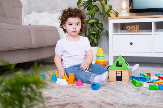 Fille enfant bouclée jouant avec pyramide et constructeur à la maison développement de la petite enfance