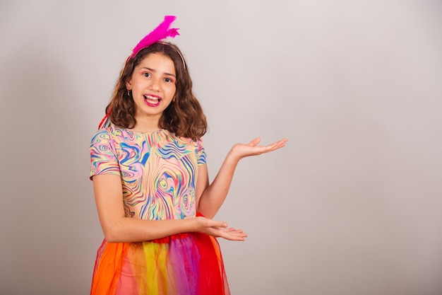 Fille enfant brésilienne vêtue d'une tenue de carnaval présentant quelque chose sur le côté de la publicité