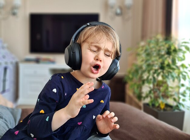 Fille enfant dans les écouteurs chante émotionnellement une chanson à la maison
