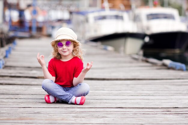 Fille enfant drôle assis à la jetée de la mer porter des vêtements décontractés