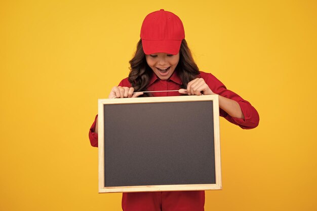 Fille enfant excitée en uniforme rouge et casquette tenir tableau noir