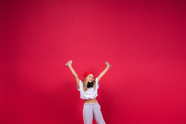 Fille enfant faisant des exercices de fitness avec des haltères sur fond rouge