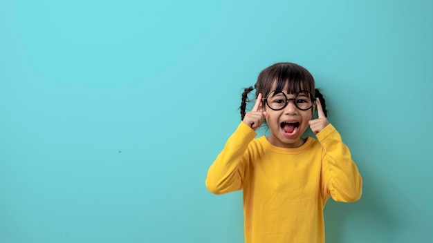 Fille enfant heureuse dans des verres pour la vue a une coiffure à la mode sur un fond vert clair