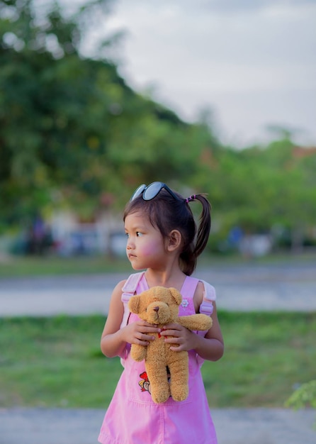 Fille enfant heureuse avec ours en peluche étreignant en robe dans le jardin d'été en plein air
