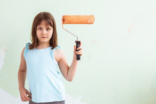 Fille enfant heureuse peint le mur avec de la peinture orange,