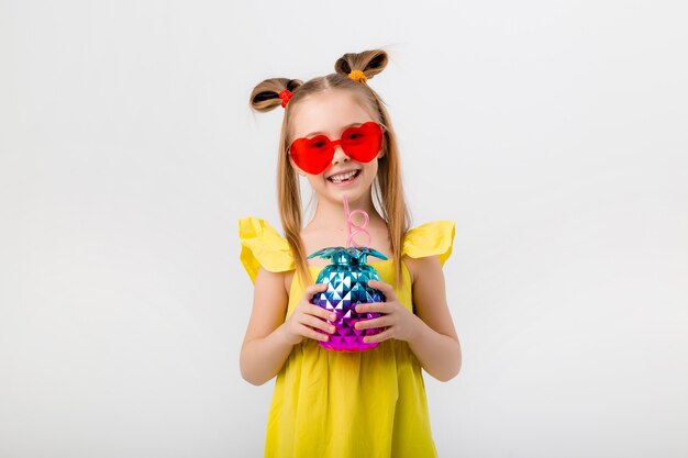 Fille enfant heureux dans des lunettes de soleil tenant un verre avec un cocktail isolat