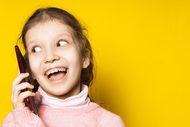 Fille. Enfant heureux parlant au téléphone sur un fond jaune. Jolie fille intelligente.