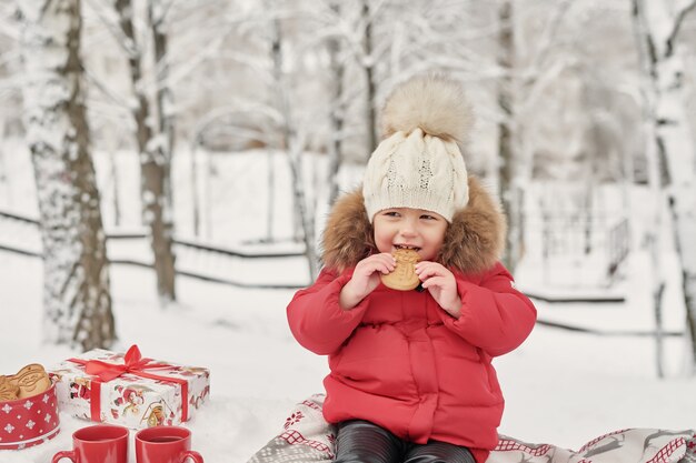 Fille enfant heureux sur la promenade d'hiver à l'extérieur de boire du thé. bébé souriant petit enfant jouant dans les vacances de Noël d'hiver. Famille de Noël à winter park. Fille dans la forêt d'hiver.