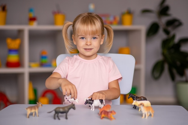 Fille enfant jouant avec des animaux jouets à la table à la maternelle ou à la maison