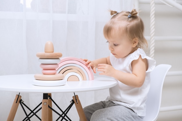 Fille enfant jouant avec un jouets en bois à table. Petite fille mignonne avec des jouets naturels.