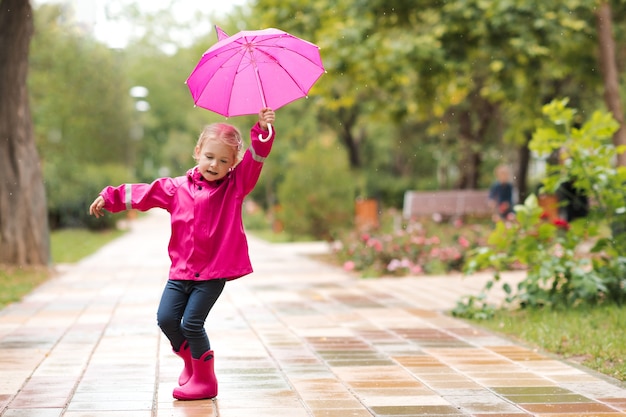 Fille d'enfant marchant sur la flaque d'eau dans le parc tenant le parapluie rose