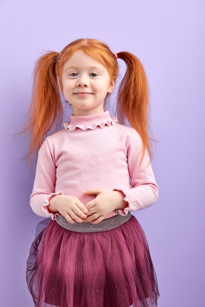 Fille enfant rousse timide et diligente avec deux queues de cheval posant, souriante, incroyable fille en jupe isolée