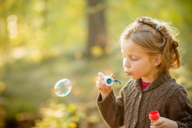 Fille enfant soufflant des bulles de savon en plein air au coucher du soleil.