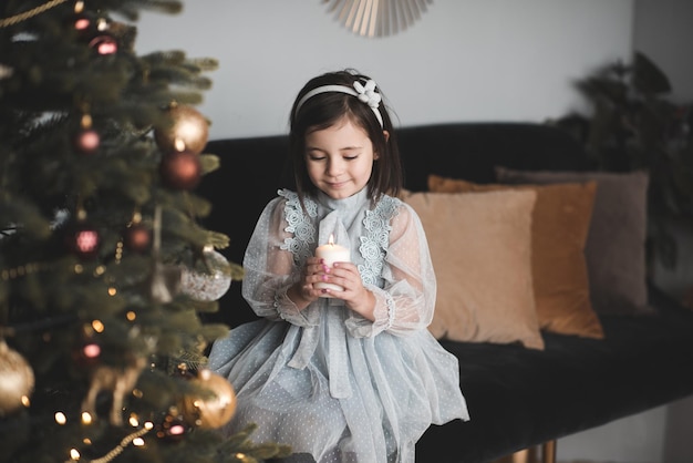 Fille enfant souriante assise sous l'arbre de Noël avec des décorations