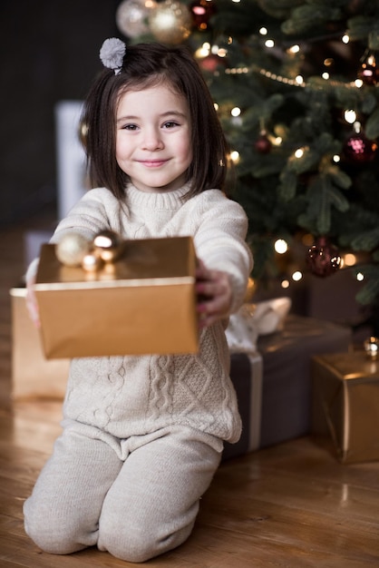 Fille enfant souriante assise sous l'arbre de Noël avec des décorations