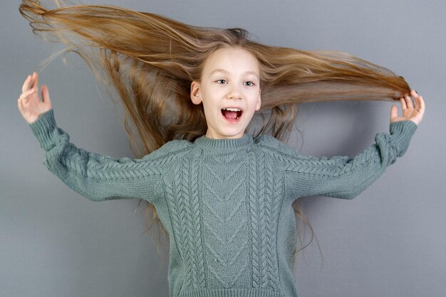 Fille enfant souriante avec de beaux longs cheveux rouges volants sur fond gris