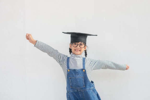 Fille d'enfants portant une casquette diplômée sur fond blanc très heureuse et excitée