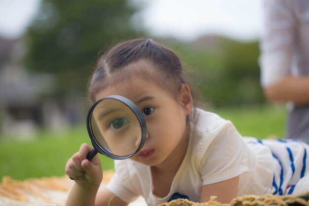 La fille d'enfants regarde des feuilles d'arbre par la pousse extérieure de loupe