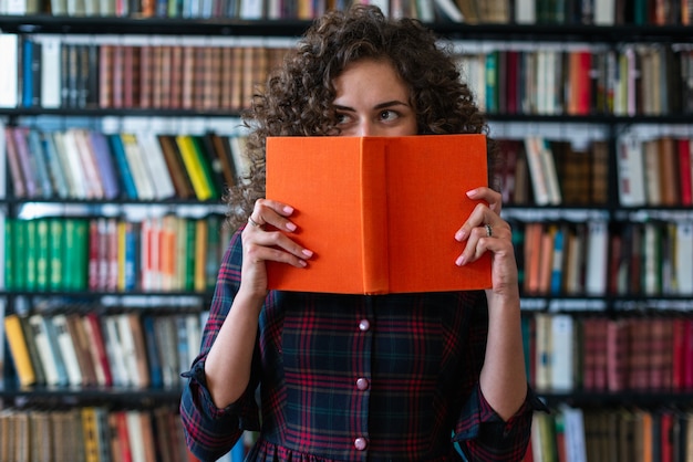 Fille enjouée tenant un livre couvrant son visage et regardant de côté. Livre à couverture rigide