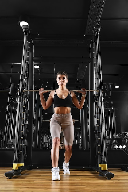 Une fille entraîne ses jambes dans la salle de sport avec une haltère. foncé