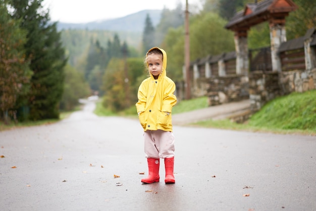 Fille espiègle portant un imperméable jaune en sautant dans une flaque d'eau pendant la pluie Enfance heureuse