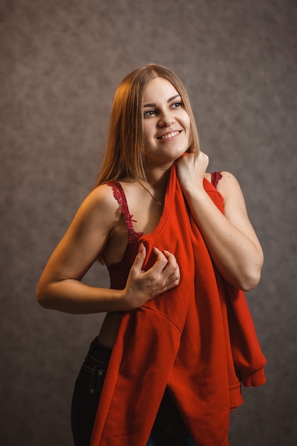 La fille essaie un pull rouge sur fond gris