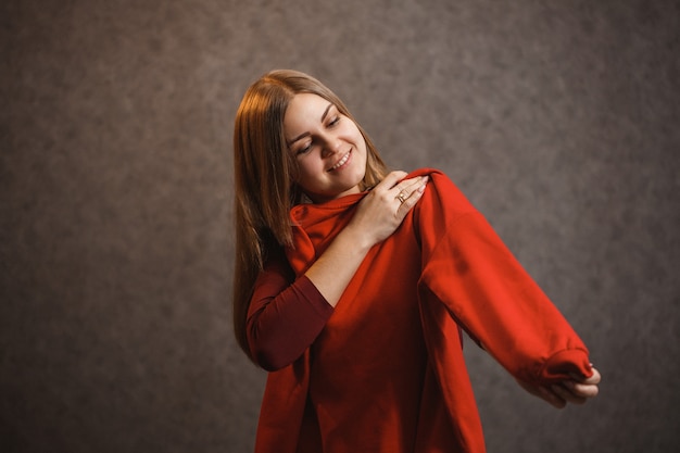 La fille essaie un pull rouge sur fond gris