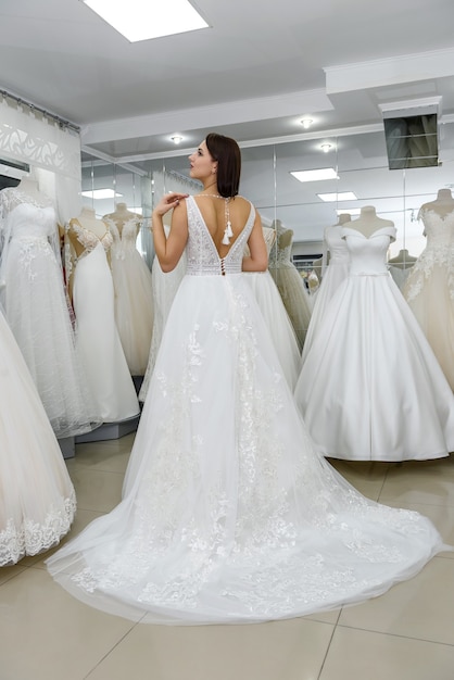 Fille essayant sur la robe de mariée dans le salon, debout en arrière