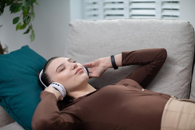 La fille est allongée sur le canapé et écoute de la musique les yeux fermés.