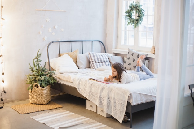 la fille est allongée sur le canapé et lit un livre, la chambre est décorée pour Noël