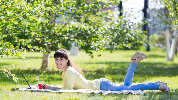 La fille est allongée sur l'herbe et tient un verre de jus.