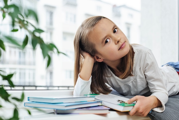 La fille est allongée sur le rebord de la fenêtre avec un livre.