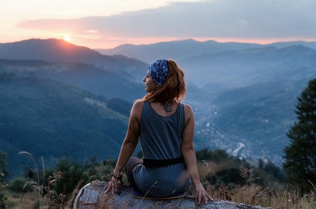 Une fille est assise au bord de la falaise et regarde la vallée du soleil et les montagnes Femme assise au sommet d'une montagne et contemplant le coucher du soleil Coucher de soleil dans les Carpates ukrainiennes