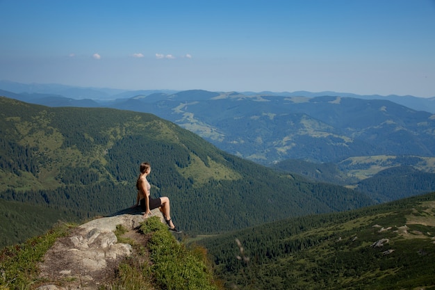 Une Fille Est Assise Au Bord De La Falaise Et Regarde La Vallée Du Soleil Et Les Montagnes.