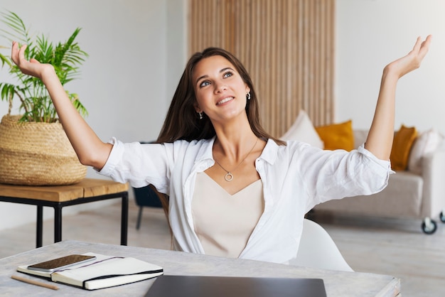 Fille est assise au bureau dans le bureau à domicile et montre un geste joyeux avec ses mains.