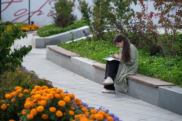 Une fille est assise sur un banc dans la rue avec des documents dans les mains et utilise son téléphone