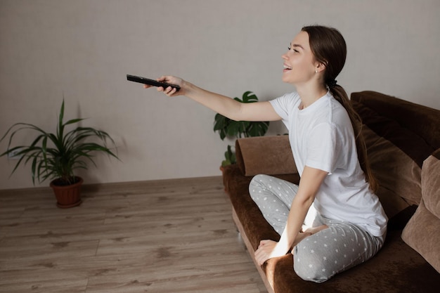 La fille est assise sur le canapé, regardant la télévision avec un sourire sur son visage.