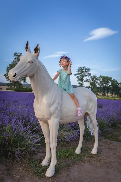 Une fille est assise sur un cheval décoratif au milieu d'un champ de lavande