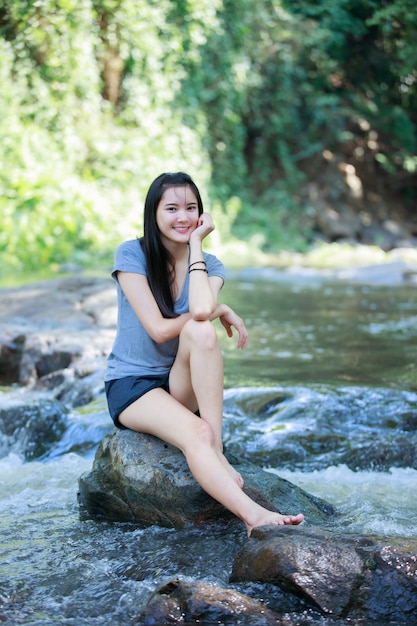 La fille est assise à une chute d&#39;eau et sourit joyeux, foyer flou et flou